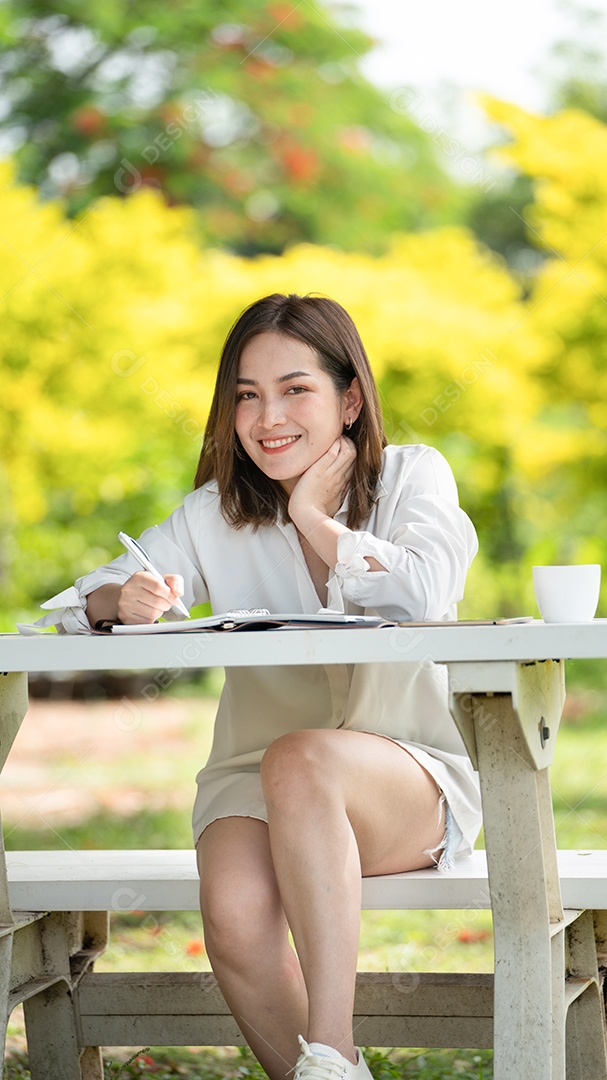 Mulher de sorriso pensativo no parque usando laptop e escrevendo.
