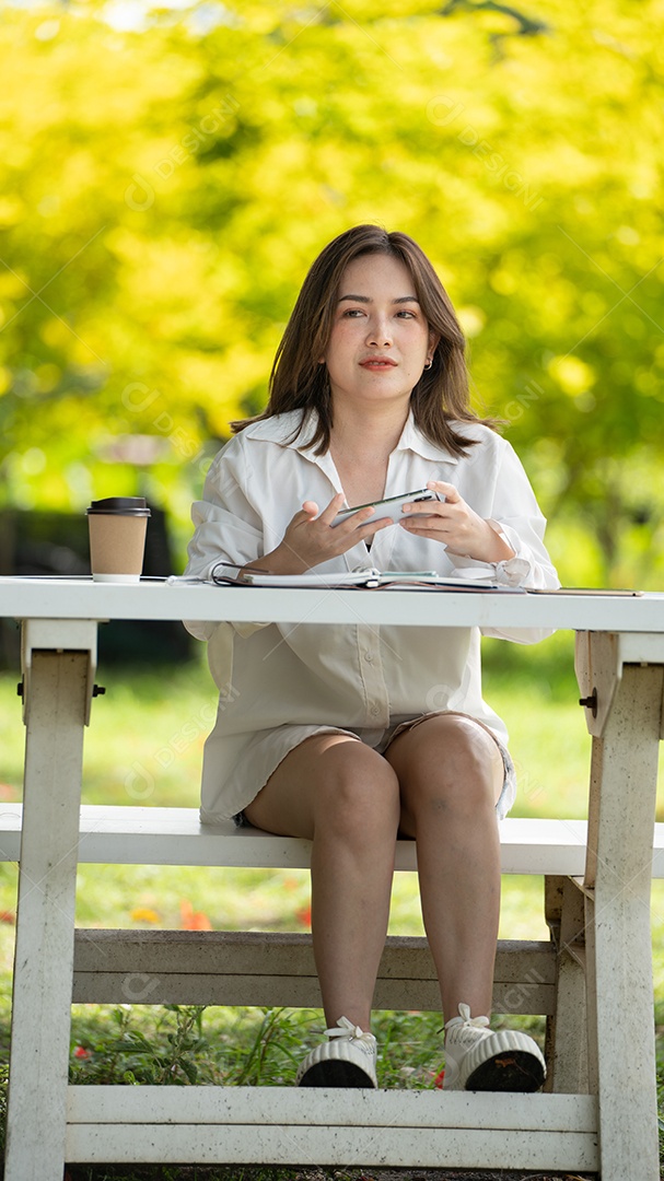 Mulher de sorriso pensativo no parque usando telefone inteligente.