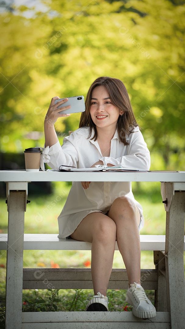 Mulher de sorriso pensativo no parque usando telefone inteligente para foto de selfie.