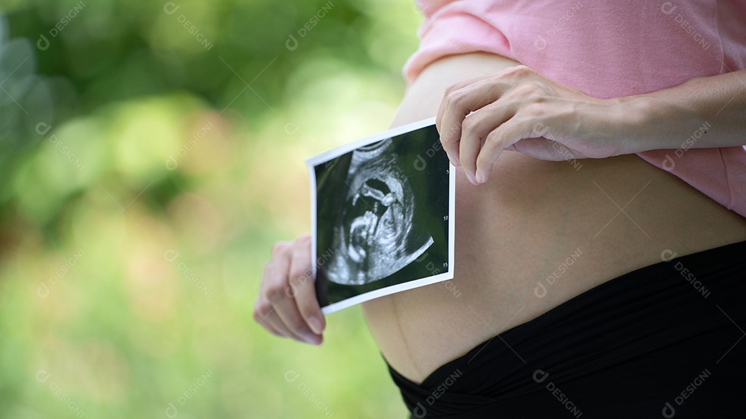 Mulher grávida asiática mostra com bebê de ultrassom, grávida relaxando no parque verde.