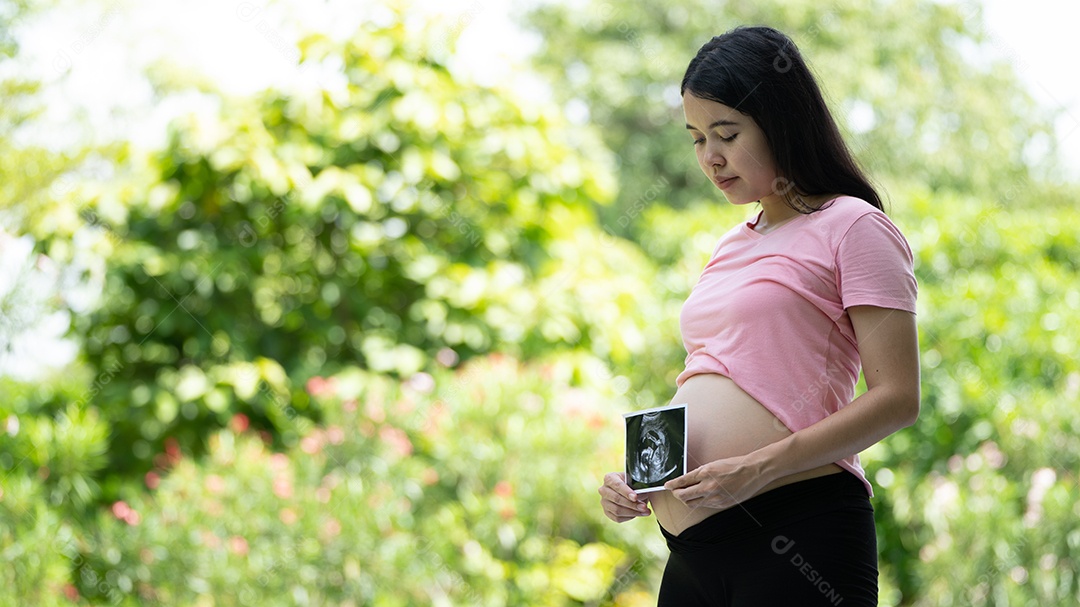 Mulher grávida asiática mostra com bebê de ultrassom, grávida relaxando no parque verde.
