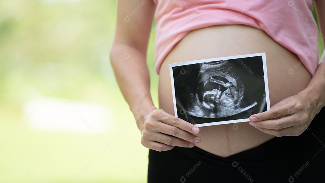 Mulher grávida asiática mostra com bebê de ultrassom, grávida relaxando no parque verde.