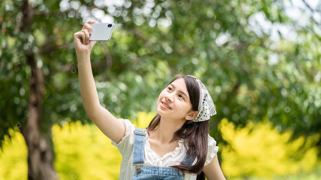 Mulher de sorriso pensativo no parque usando telefone inteligente para foto de selfie.