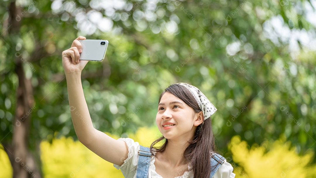 Mulher de sorriso pensativo no parque usando telefone inteligente para foto de selfie.