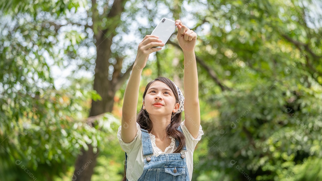 Mulher de sorriso pensativo no parque usando telefone inteligente para foto de selfie.