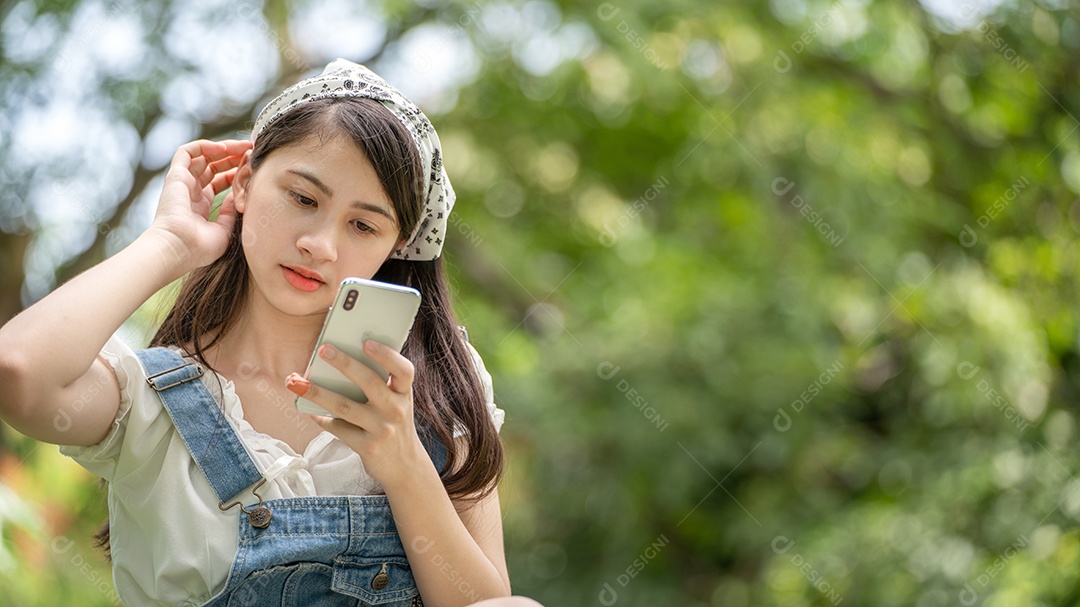 Mulher de sorriso pensativo no parque usando telefone inteligente.