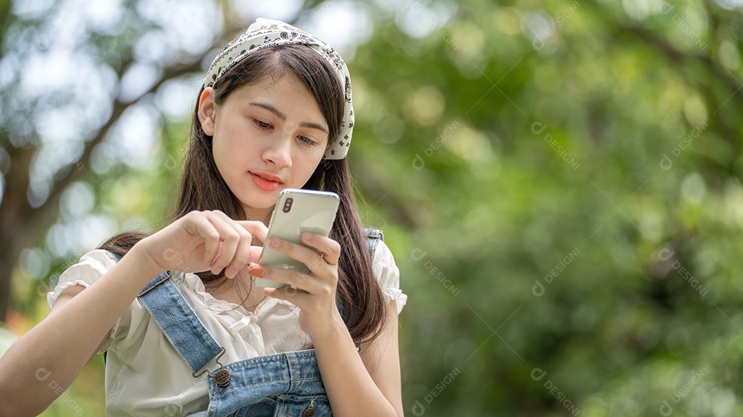 Mulher de sorriso pensativo no parque usando telefone inteligente.