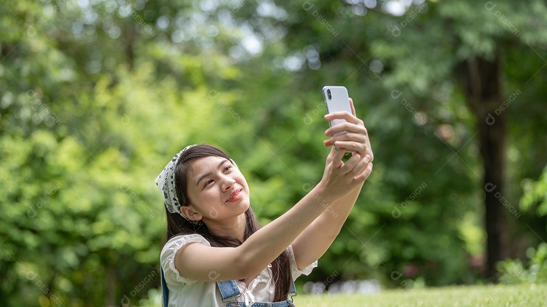 Retrato de menina tirando foto com celular e fazendo gestos no parque verde da cidade verde em spri