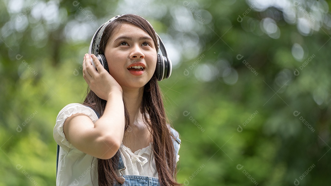 Retrato de menina com fones de ouvido fazendo gestos no parque verde da cidade verde em spri