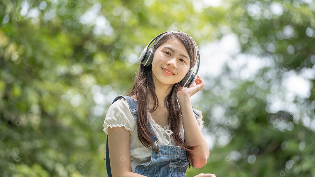 Retrato de menina com fones de ouvido fazendo gestos no parque verde da cidade verde em spri