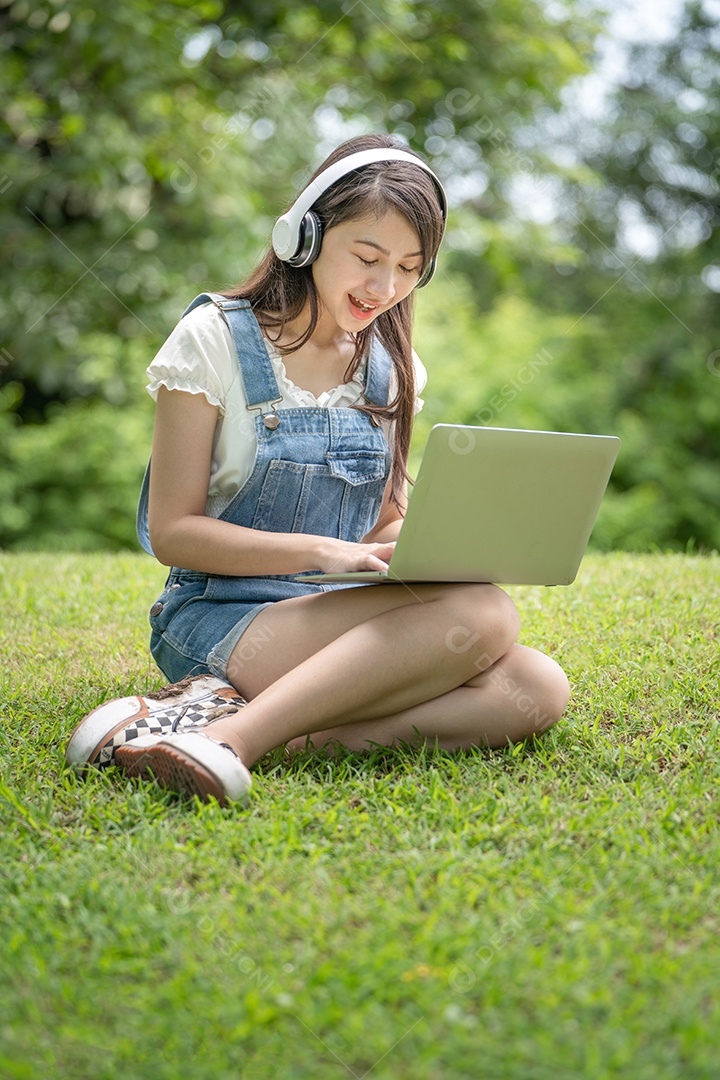 Retrato de menina com fones de ouvido e mexendo em notebook fazendo gestos no parque verde da cidade verde em spri