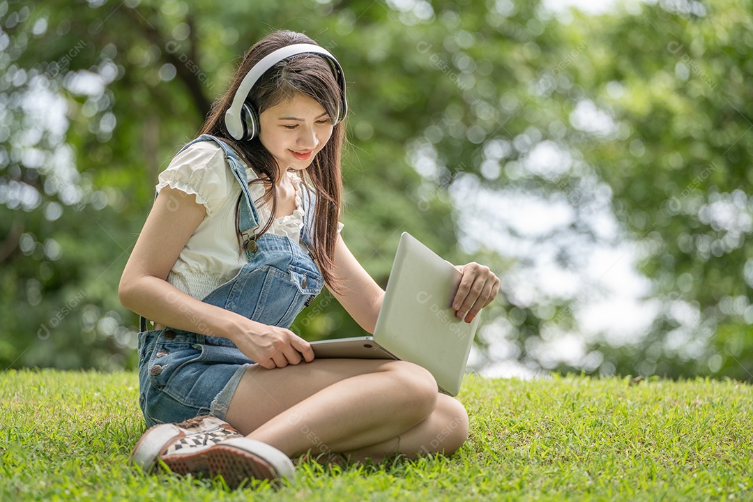 Retrato de menina com fones de ouvido e mexendo em notebook fazendo gestos no parque verde da cidade verde em spri