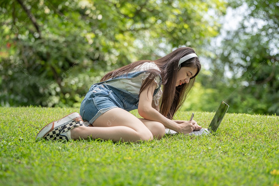 Retrato de menina com fones de ouvido e mexendo em notebook fazendo gestos no parque verde da cidade verde em spri