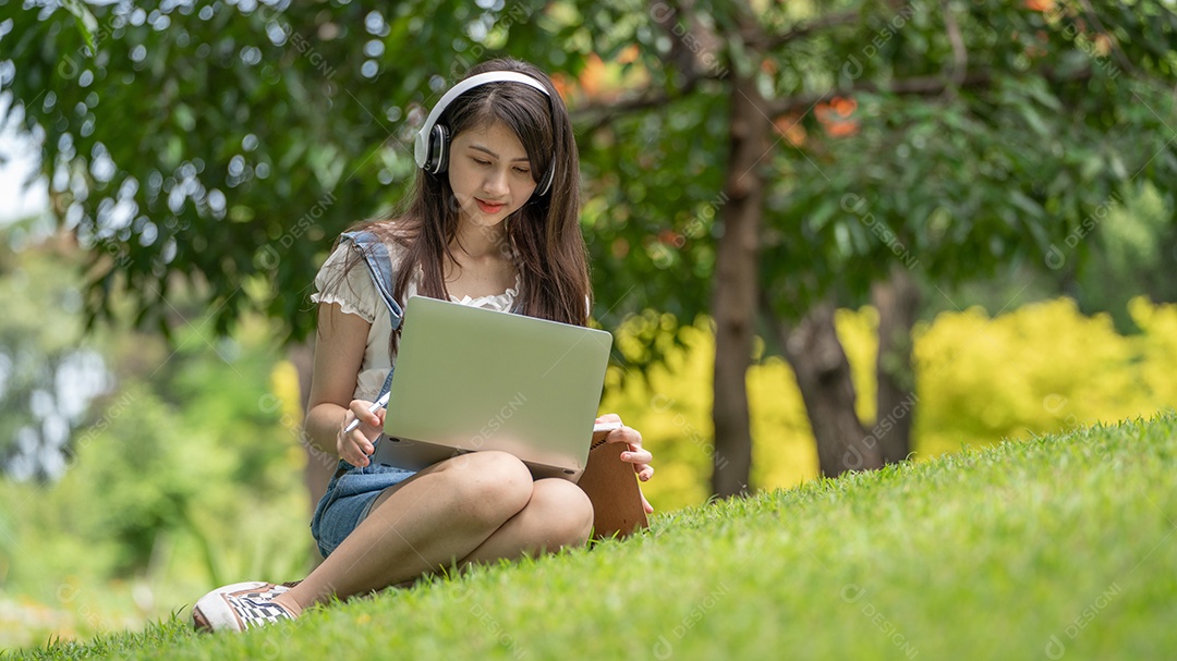 Retrato de menina com fones de ouvido e mexendo no notebook fazendo gestos no parque verde da cidade verde em spri