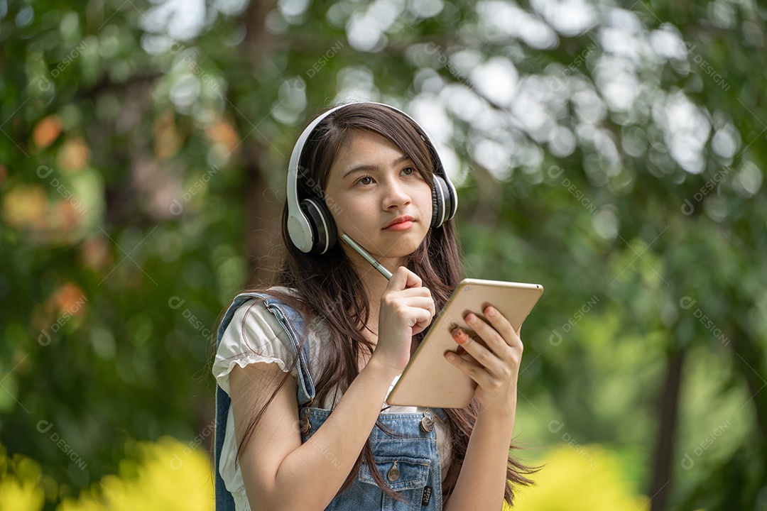 Retrato de menina com fones de ouvido e segurando tablet fazendo gestos no parque verde da cidade verde em spri