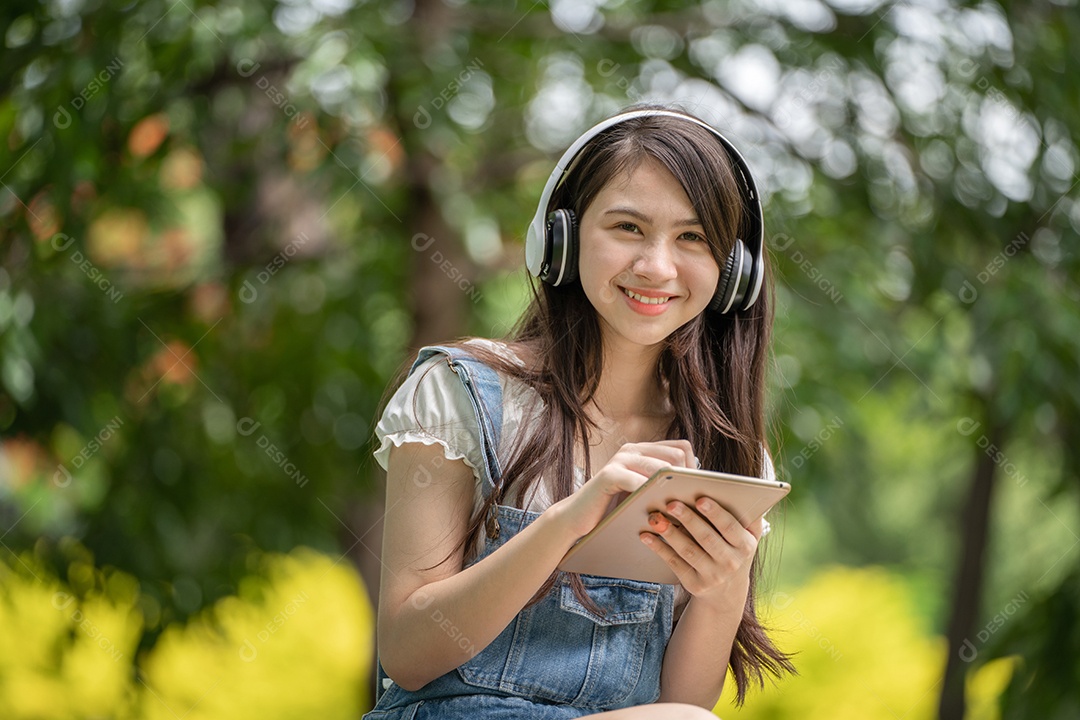 Retrato de menina com fones de ouvido e segurando tablet fazendo gestos no parque verde da cidade verde em spri