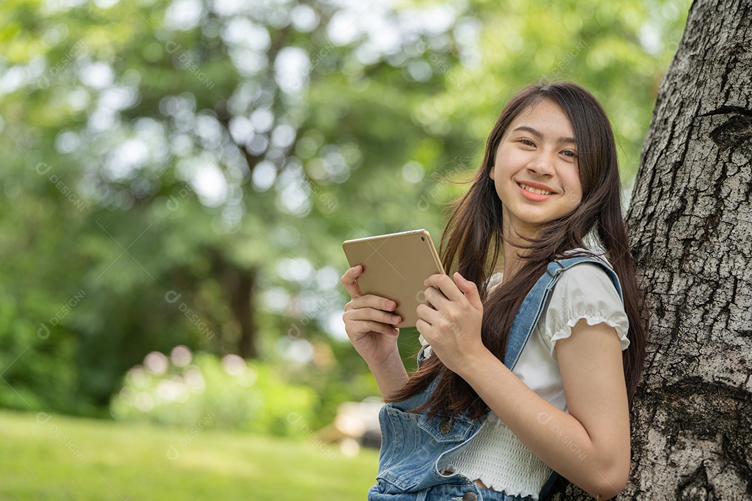 Retrato de menina segurando tablet fazendo gestos no parque verde da cidade verde em spri