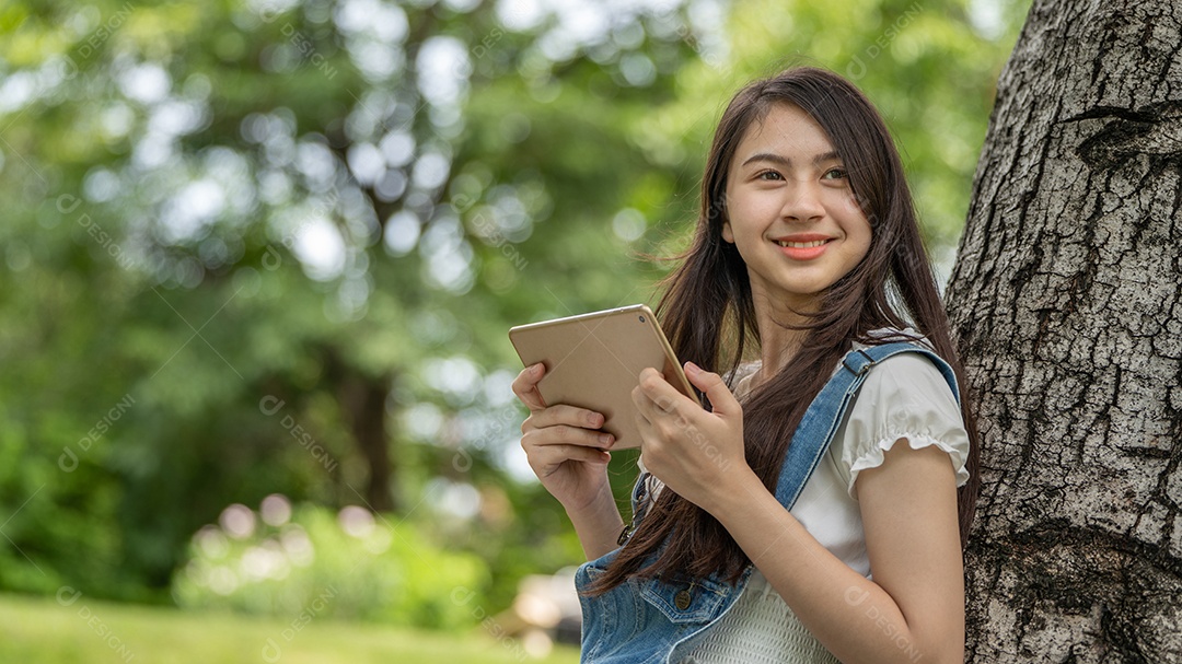 Retrato de menina segurando tablet fazendo gestos no parque verde da cidade verde em spri