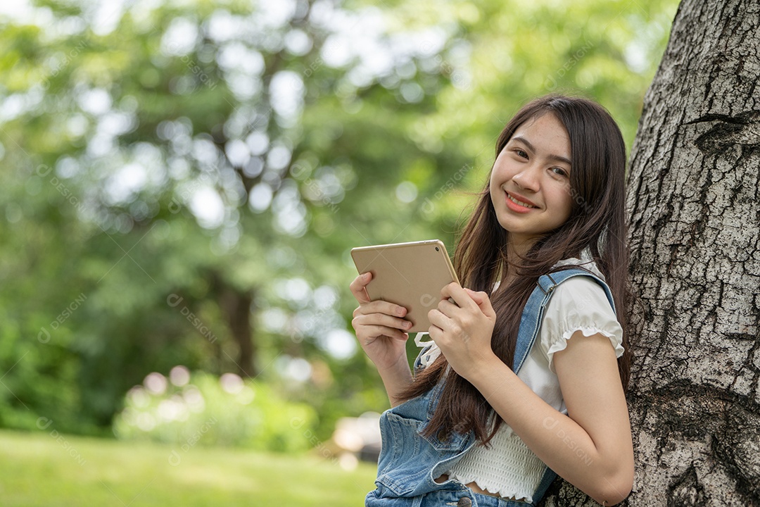 Retrato de menina segurando tablet fazendo gestos no parque verde da cidade verde em spri