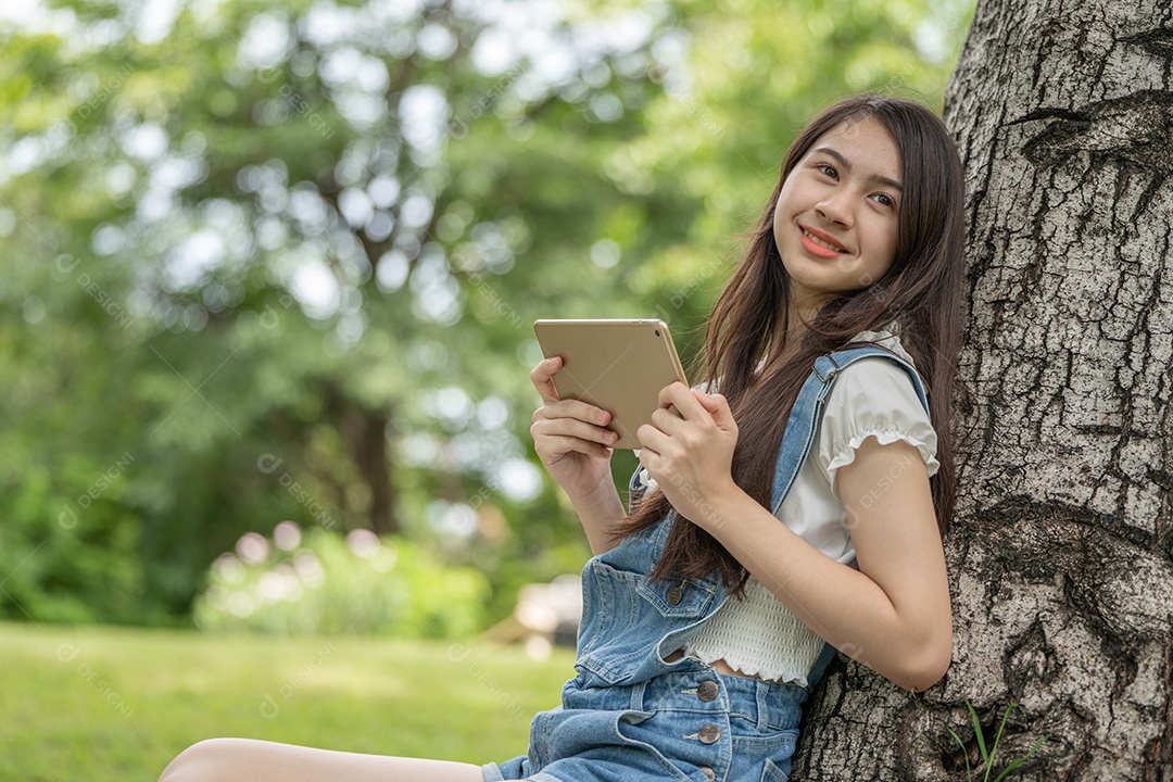 Retrato de menina segurando tablet fazendo gestos no parque verde da cidade verde em spri