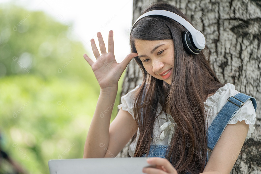 Retrato de menina com fones de ouvido e segurando tablet fazendo gestos no parque verde da cidade verde em spri