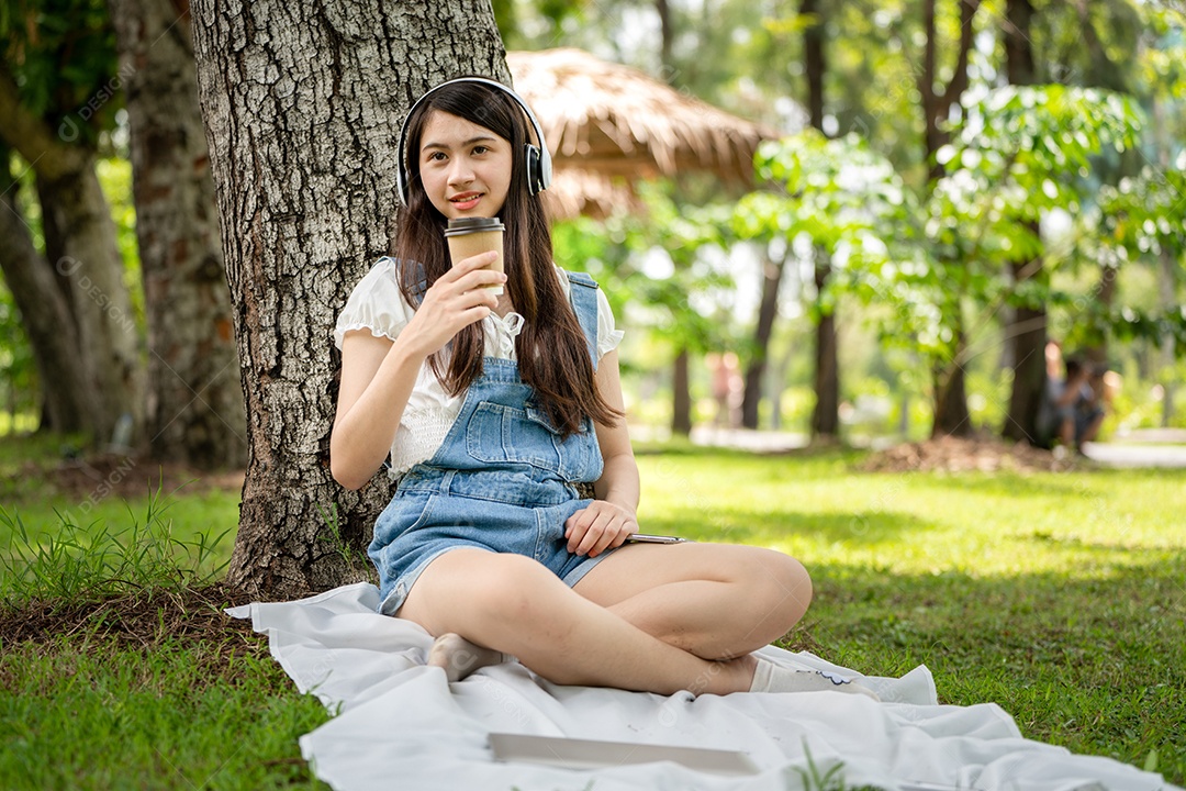 Retrato de menina com fones de ouvido e segurando copo de café fazendo gestos no parque verde da cidade verde em spri