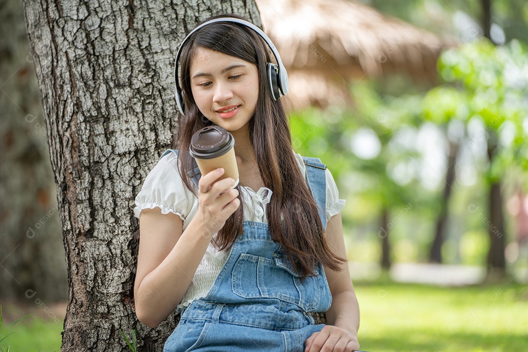 Retrato de menina com fones de ouvido e segurando copo de café fazendo gestos no parque verde da cidade verde em spri