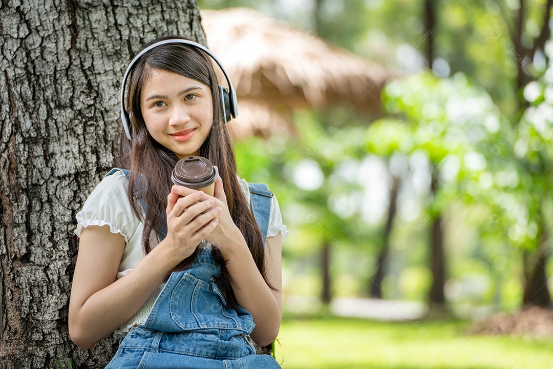 Retrato de menina com fones de ouvido e segurando copo de café fazendo gestos no parque verde da cidade verde em spri