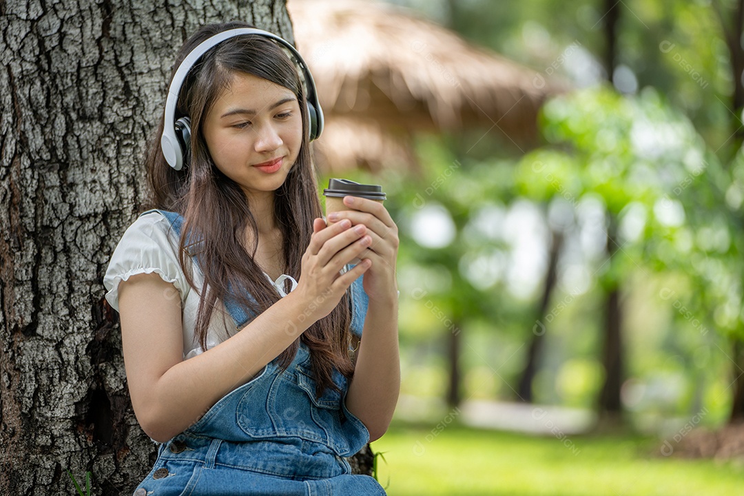 Retrato de menina com fones de ouvido e segurando copo de café fazendo gestos no parque verde da cidade verde em spri