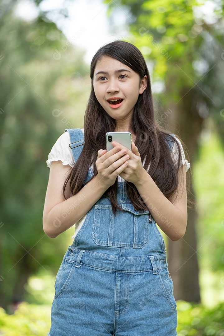 Retrato de menina segurando um celular fazendo gestos no parque verde da cidade verde em spri