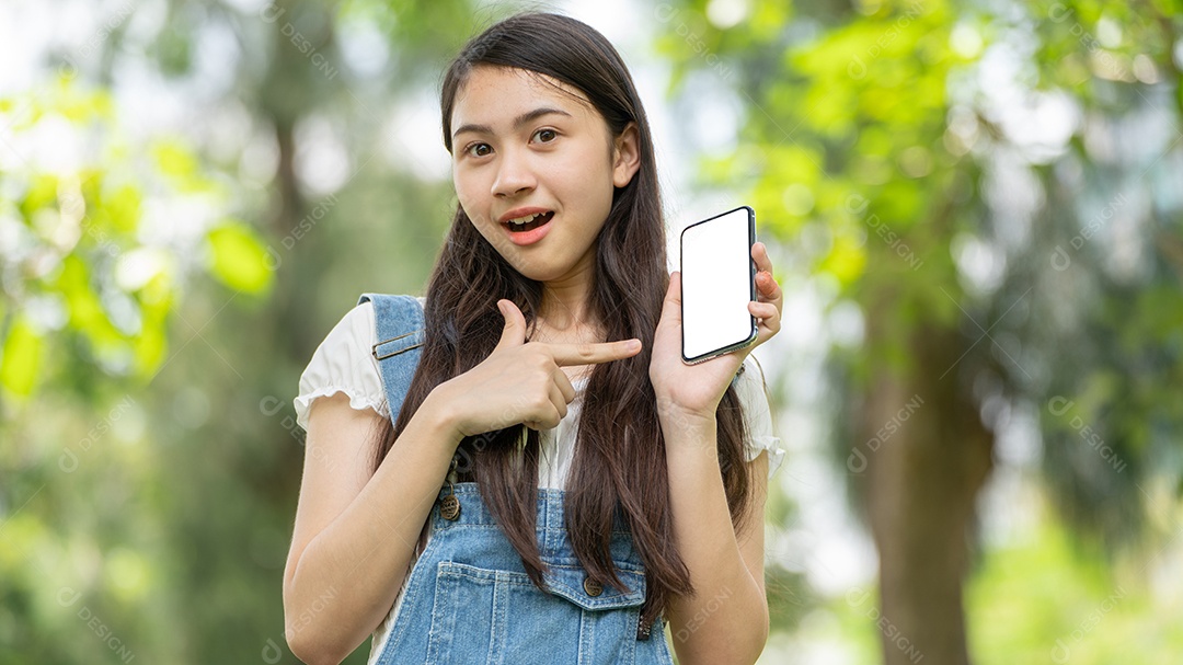 Retrato de menina segurando um celular fazendo gestos no parque verde da cidade verde em spri