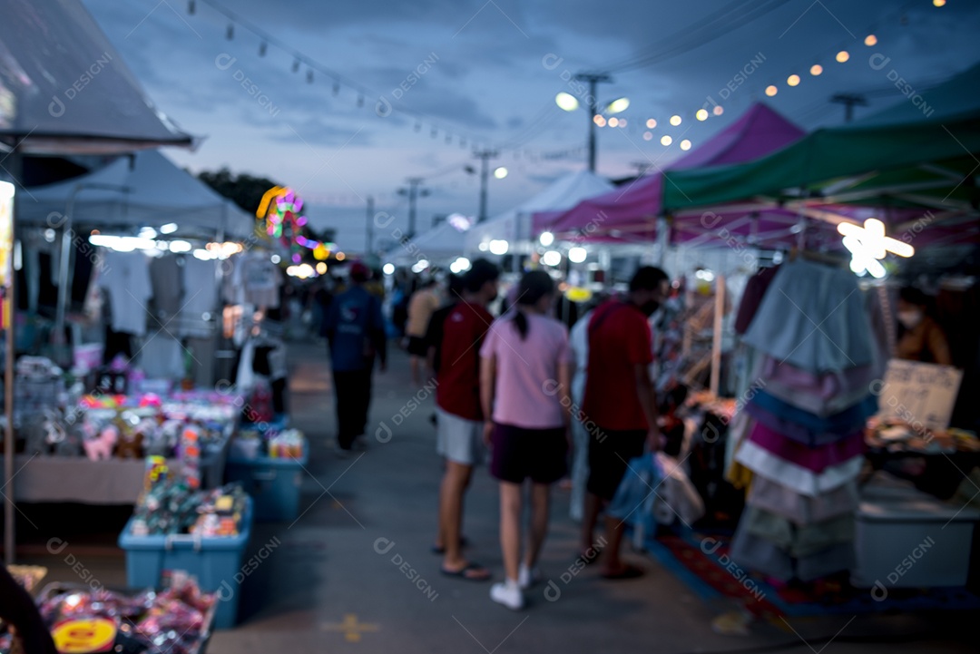 Imagem borrada de pessoas do festival do mercado noturno andando na estrada com luz bokeh para segundo plano.