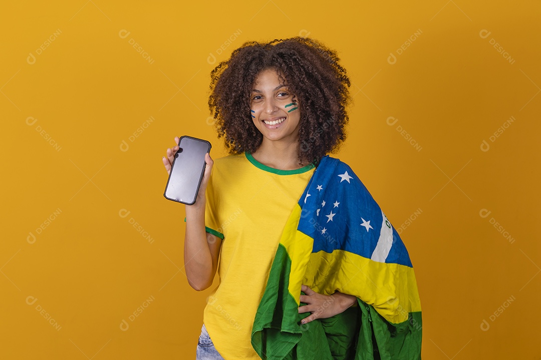 Mulher afro-brasileira vestindo camiseta do Brasil e segurando um smartphone celular