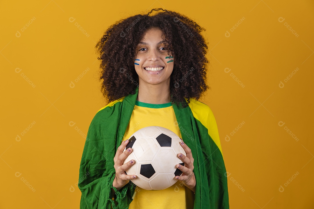 Mulher afro-brasileira vestindo camiseta do Brasil e segurando uma bola de futebol