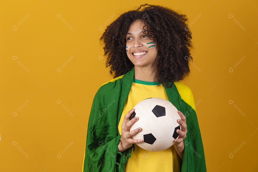 Mulher afro-brasileira vestindo camiseta do Brasil e segurando uma bola de futebol