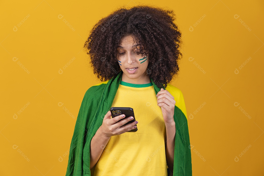 Mulher afro-brasileira vestindo camiseta do Brasil e segurando um smartphone celular