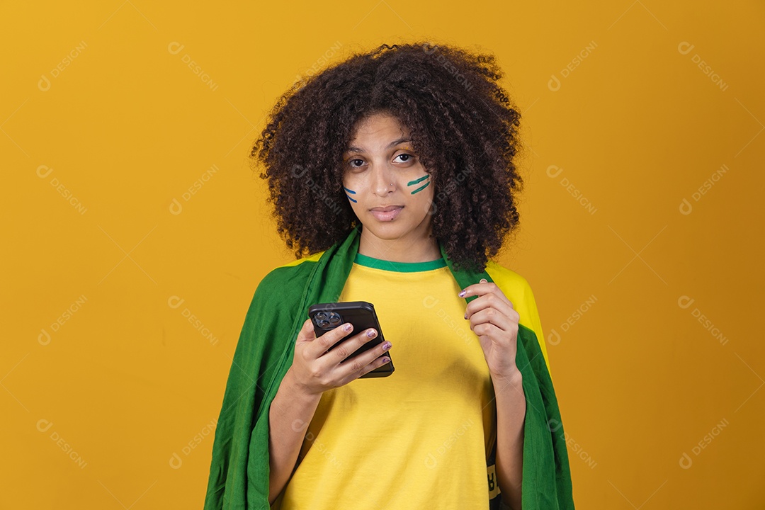 Mulher afro-brasileira vestindo camiseta do Brasil e segurando um smartphone celular