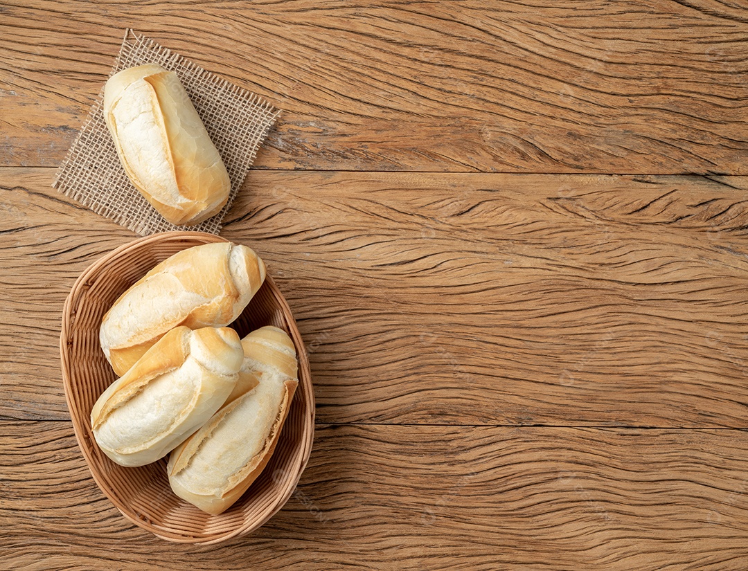 Pão francês integral, pão de sal ou pistolet em uma tigela sobre a mesa de madeira.