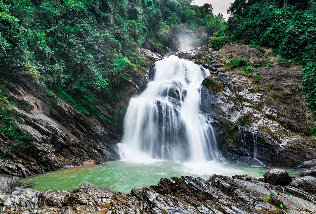 Linda cachoeira na montanha com céu azul e nuvens brancas.