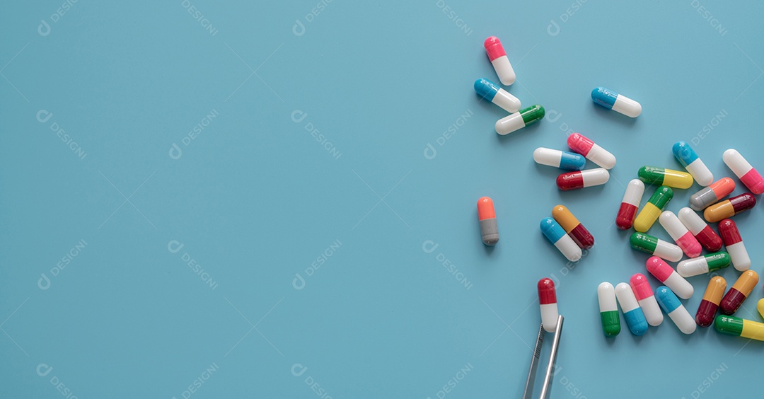 Comprimidos de cápsulas de antibióticos na colher e fundo azul.