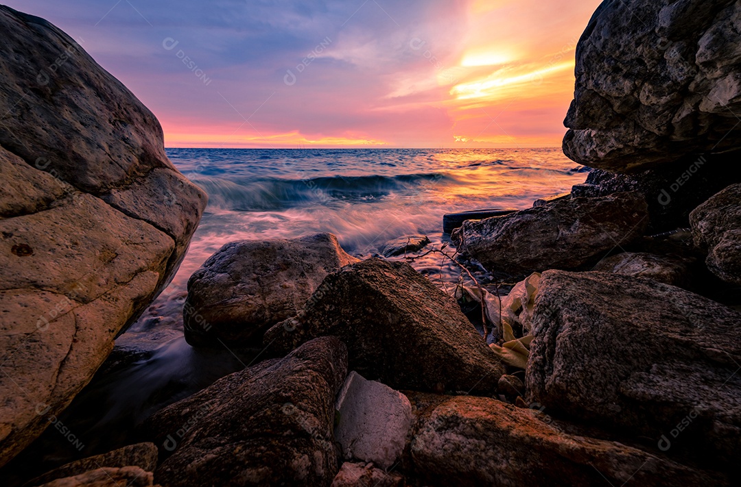 Salpicos de água do oceano na praia rochosa com céu pôr do sol rosa e dourado