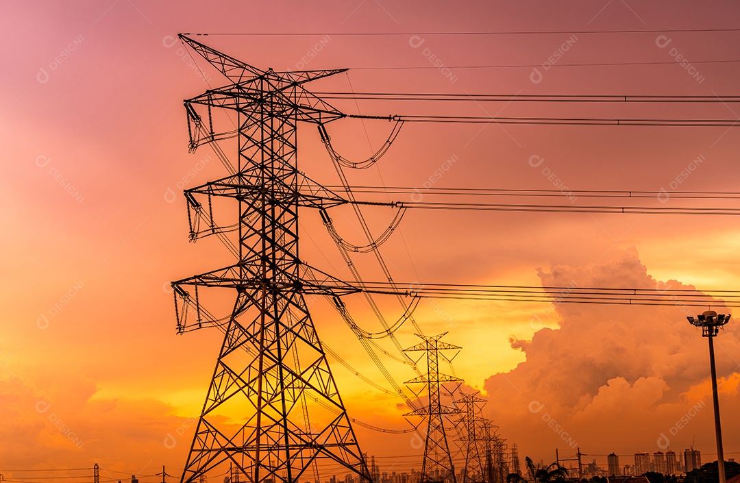 Pilões elétricos de alta tensão e linhas de transmissão com céu pôr do sol laranja
