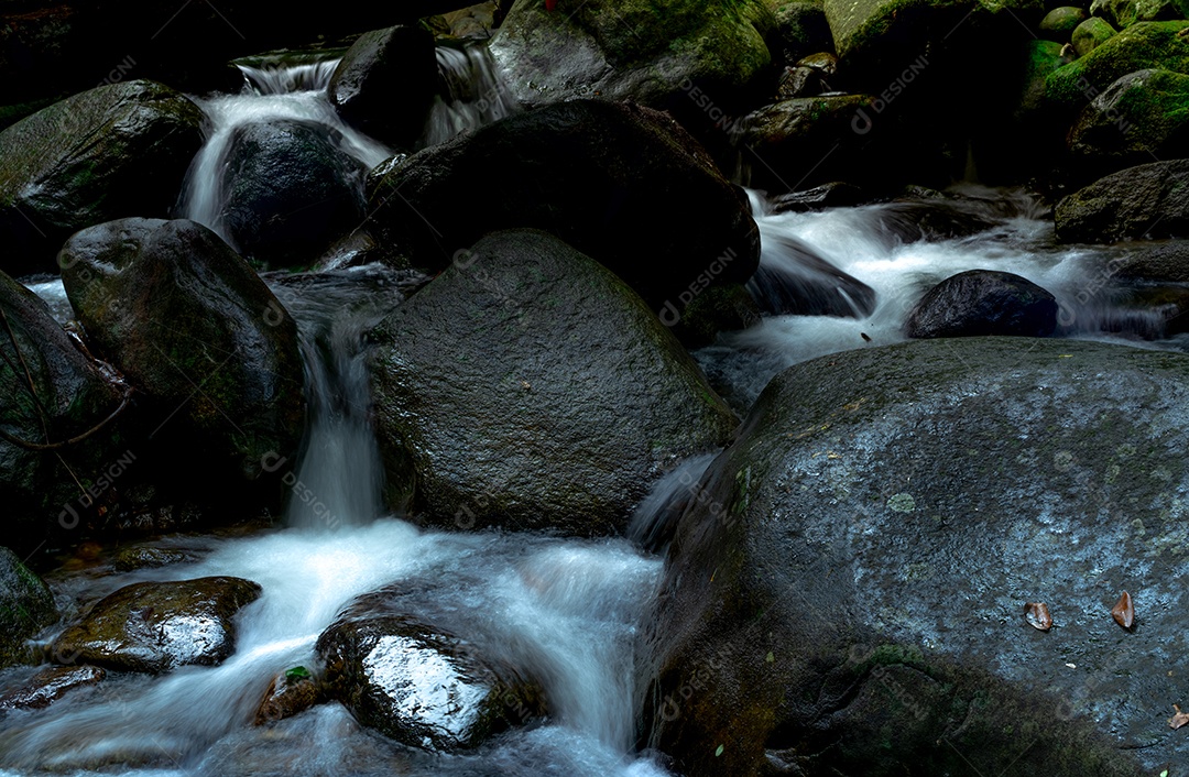 Rocha negra na cachoeira com musgo verde e sol na rocha.