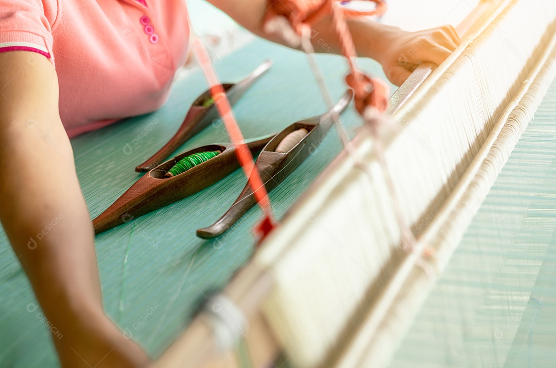 Mulher que trabalha na máquina de tecelagem para tecer tecido artesanal.