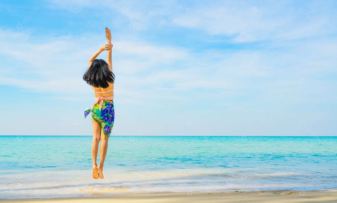 Mulher jovem feliz em traje de banho pulando na praia de areia.