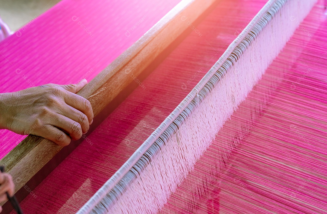 Mulher que trabalha na máquina de tecelagem para tecer tecido artesanal.