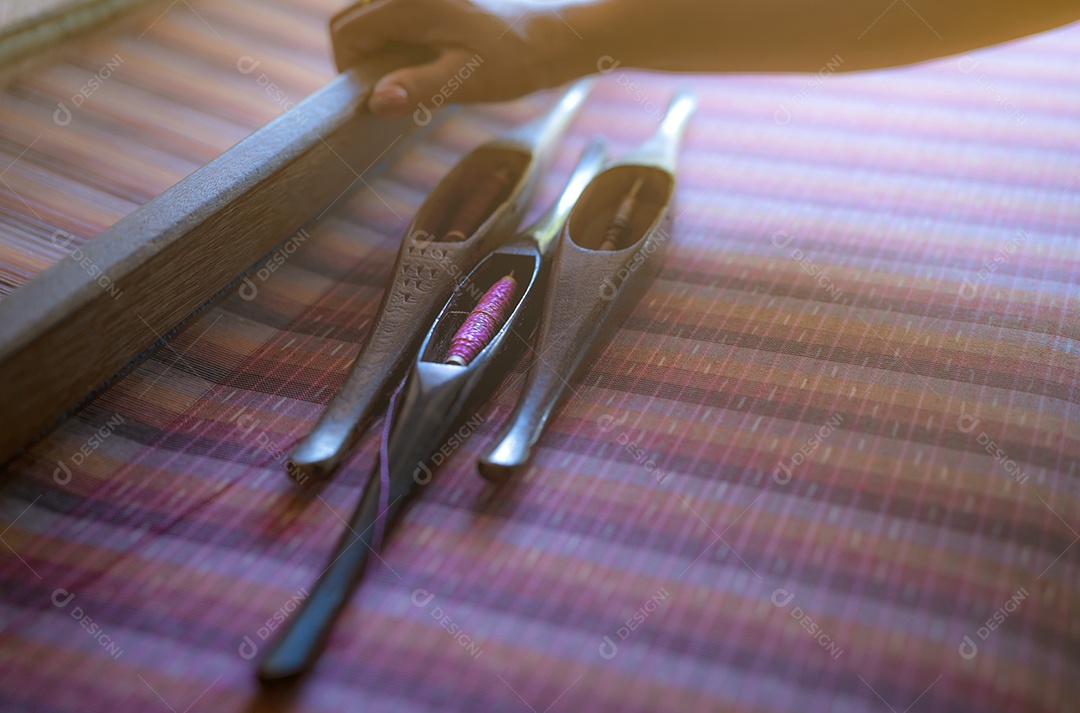 Mulher que trabalha na máquina de tecelagem para tecer tecido artesanal.