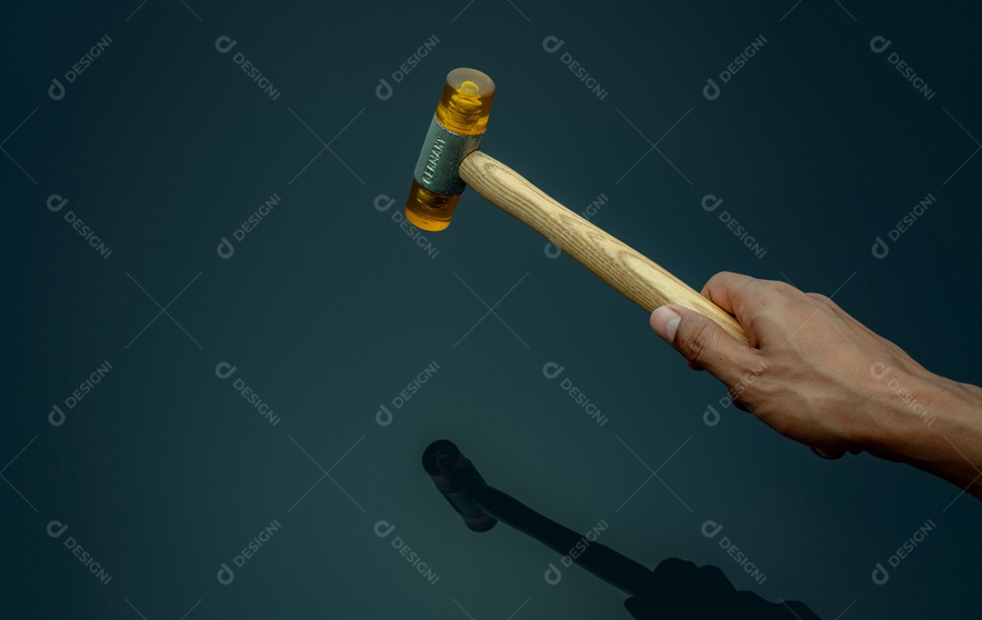 A mão segurando o martelo de plástico isolado em fundo escuro.