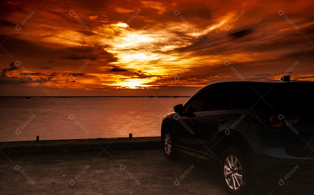 Carro SUV azul de luxo estacionado na estrada de concreto à beira-mar ao pôr do sol