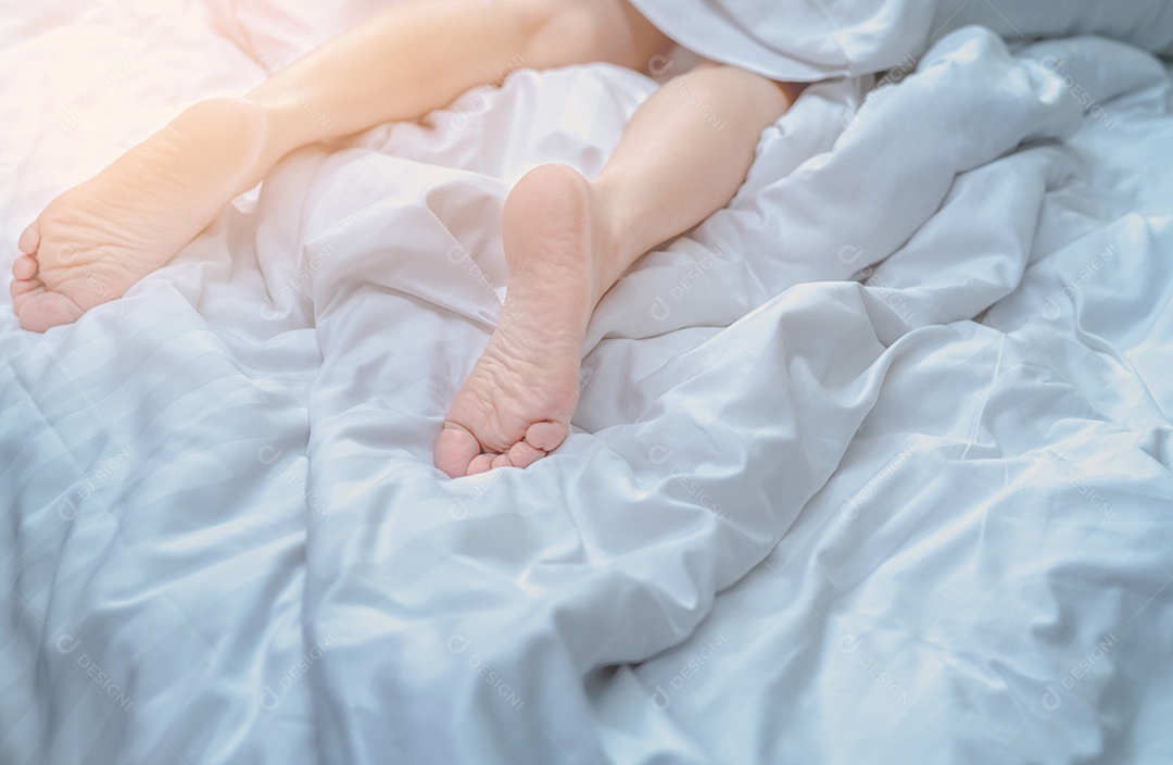 Mulher com os pés descalços na cama sobre o cobertor de linho branco